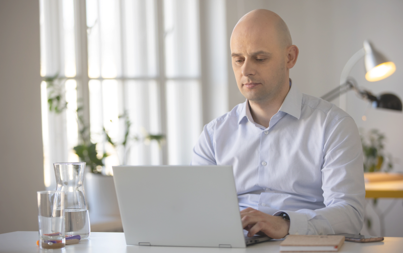 Mężczyzna w niebieskiej koszuli skupiony wzrokiem zerka w ekran laptopa.